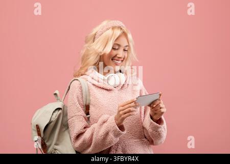 Giovane donna felice che sorride mentre usa uno smartphone, sfondo rosa chiaro Foto Stock