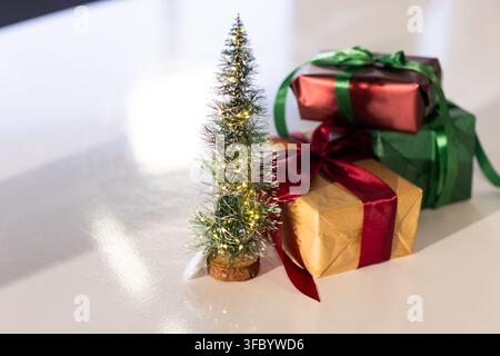 Albero di Natale in miniatura con luci calde in lamelle sopra il tavolo accanto a scatole regalo metalliche Foto Stock
