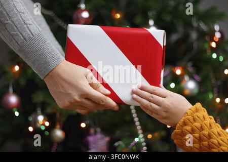 Mamma regala un regalo al bambino sullo sfondo di un albero di Natale con le luci Foto Stock