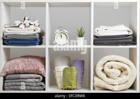 Organizzazione dello stoccaggio. Pile di asciugamani, lenzuola, biancheria da letto, coperte e cuscini su uno scaffale bianco Foto Stock