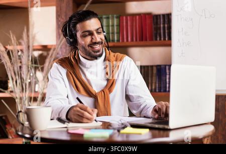 Insegnante indiano allegro al laptop che insegna in linea che siede a casa Foto Stock