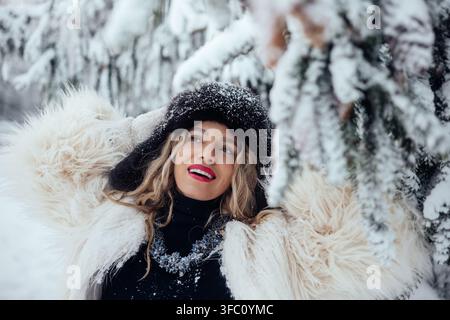 Usita invernale con una donna che si gode la neve nella foresta sotto alberi coperti di neve Foto Stock