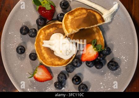 Un vortice di panna montata corona pancake dorati circondati da mirtilli e fragole freschi. Foto Stock