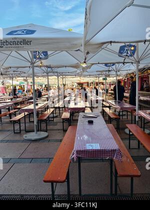 Pforzheim Germania 23 agosto 2026 Oechsle Fest Pforzheim Scena vivace in un birreria all'aperto con lunghe panchine di legno, tavoli coperti di gingham, ombrellone bianco Foto Stock