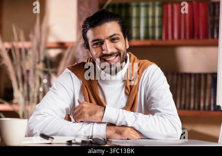 Ritratto di giovane insegnante arabo seduto al posto di lavoro al chiuso Foto Stock