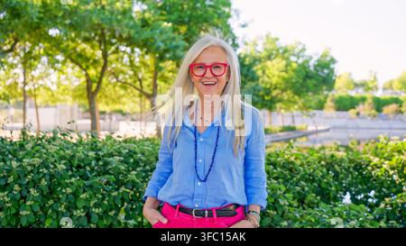 Donna sorridente con occhiali rossi in piedi nel parco Foto Stock