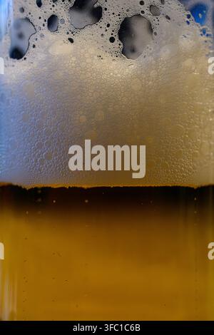 Un primo piano dettagliato che cattura la texture di una birra dorata in un bicchiere, con uno spesso strato di schiuma bianca e spumosa e numerose piccole bolle visibili Foto Stock