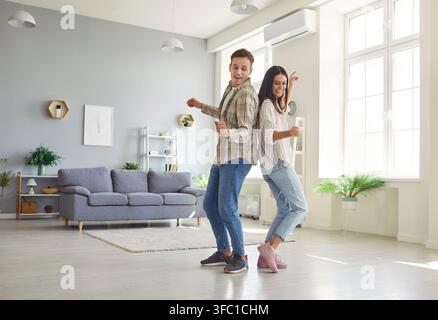Gioiosa giovane coppia familiare che si diverte e balla insieme nell'interno del soggiorno Foto Stock