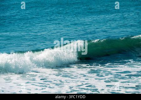 Un primo piano di un'onda turchese vibrante che si infrange e si trasforma in schiuma bianca sul mare contro uno sfondo di acqua blu profonda che ondeggia. Foto Stock