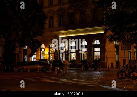 Esterno illuminato del Cafe Savoy con posti a sedere all'aperto e auto parcheggiate durante la sera a Praga. Foto Stock