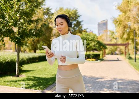 Una giovane e bella donna asiatica ascolta musica mentre cammina in un parco verde e soleggiato. Foto Stock