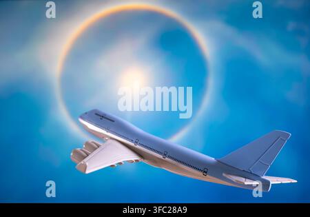 Modello di aereo Jumbo Jet generico blu chiaro e bianco che vola contro uno sfondo visualizzato su schermo di un fenomeno di alone solare luminoso Foto Stock