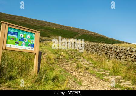Un cartello informativo "Pendle Hill ti dà il benvenuto" si trova all'inizio di un sentiero lastricato di pietra che conduce ai pendii erbosi del Pendle Hill nel Lancashire Foto Stock