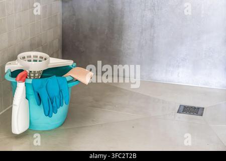 Una collezione di strumenti e prodotti per la pulizia è disposta ordinatamente su un pavimento piastrellato, pronta per l'uso Foto Stock