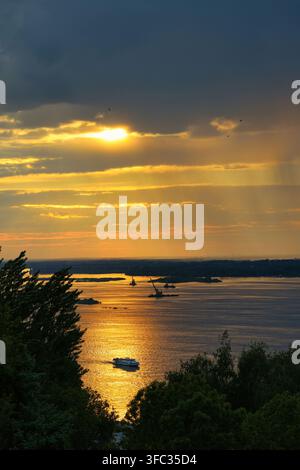 Tramonto dorato sul mare con barche e yacht silouettati sull'acqua calma, visti attraverso gli alberi da una costa elevata Foto Stock