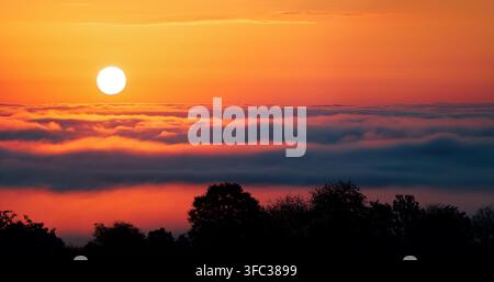 Alba calma e cielo profondamente arancione su nebbia o nuvole ondulate. Fenomeno meteorologico affascinante con bellissime colori vibranti. Foto Stock