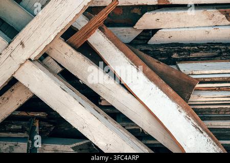 Sfondo a quadro intero di assi di legno consumate con vernice bianca scrostata che si incrociano in un cumulo di scarti di costruzione. Messa a fuoco selettiva. Foto Stock