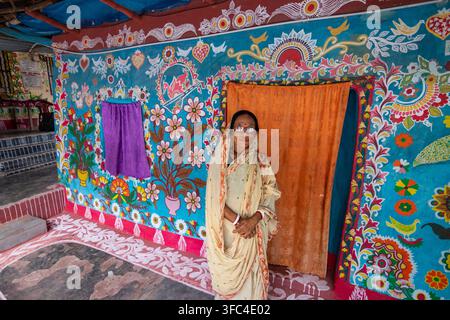 Tikoil, Bangladesh – 22 giugno 2022: Vista di una donna anziana in piedi davanti a un muro decorato con l'arte popolare tradizionale colorata Alpona ad Alpona Foto Stock