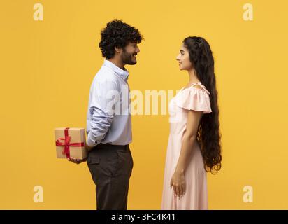 Coppia multiculturale felice che condivide un regalo, sorridente, sfondo giallo, concetto di relazione Foto Stock