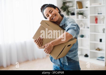 Giovane donna felice che abbraccia scatole in una casa moderna, concetto di disimballaggio Foto Stock