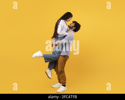 Coppia che si abbraccia in un ascensore gioioso insieme, sorridente, sfondo giallo brillante, concetto di amore e connessione Foto Stock