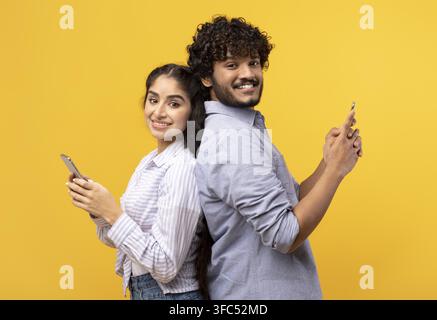 Giovane coppia felice che sorride e usa gli smartphone insieme, sfondo giallo, concetto di stile di vita Foto Stock