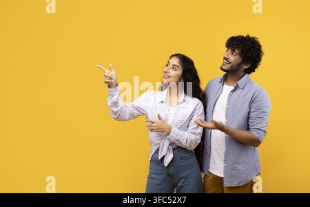 Donna e uomo sudasiatici sorridenti che indicano qualcosa in studio, sfondo giallo Foto Stock