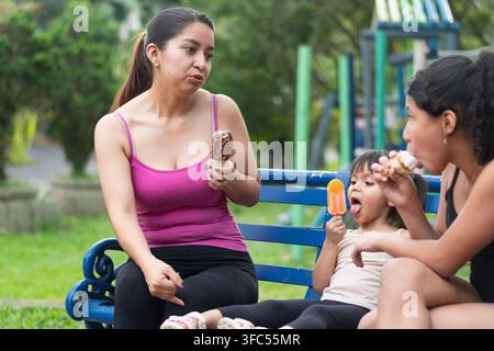 Madre latina che parla con le sue figlie mentre godono insieme del gelato nel parco Foto Stock