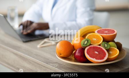 Nutrizionista che lavora su un laptop con frutti sani in clinica, concetto di perdita di peso Foto Stock