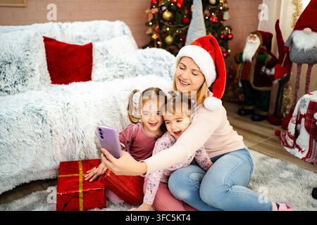 Madre e figlie felici che celebrano il Natale, scattando un selfie su uno smartphone Foto Stock