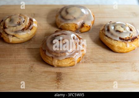 Primo piano di rotoli di cannella fatti in casa ricoperti di glassa dolce e disposti su un tagliere di legno. Pasticcini dorati appena sfornati con cannella visibile Foto Stock