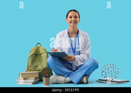 Formazione medica e carriera sanitaria, giovane dottoressa o studentessa seduta con libri e modello molecolare su sfondo blu Foto Stock