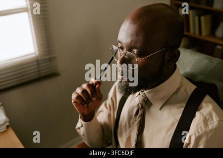 Uomo d'affari nero di mezza età pensieroso che lavora in un ufficio retrò Foto Stock