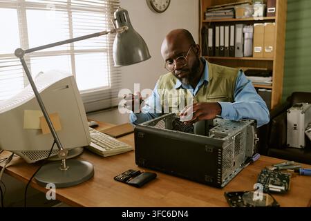 Uomo di mezza età nero che ripara un computer retrò in ufficio Foto Stock
