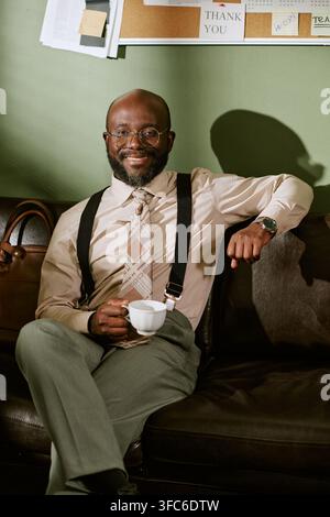 Ritratto di un uomo nero sorridente che tiene una tazza di caffè in un ufficio retrò Foto Stock