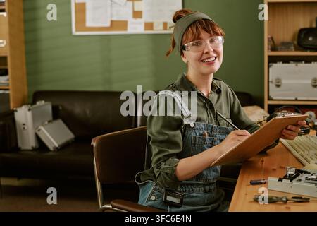 Ritratto di un'ingegnere sorridente che scrive su una clipboard in un ufficio retrò Foto Stock