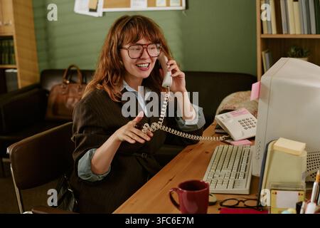 Donna sorridente al telefono in un ufficio retrò Foto Stock