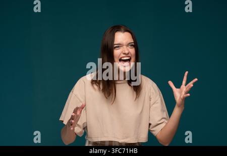 Giovane donna che mostra forti emozioni di frustrazione e rabbia, urlando ad alta voce con la bocca spalancata e mani espressive Foto Stock