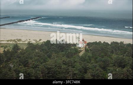 Vista aerea del faro di Yaquina Head circondato da una fitta foresta sempreverde e da una costa sabbiosa lungo l'Oceano Pacifico a Newport, Oregon, Stati Uniti Foto Stock