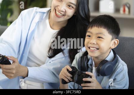 Una madre e suo figlio esprimono entusiasmo e gioia mentre giocano ai videogiochi e così mostrano il legame familiare Foto Stock