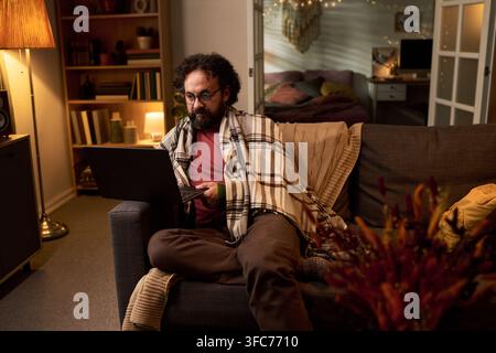Uomo di mezza età che lavora su un laptop a casa la sera Foto Stock