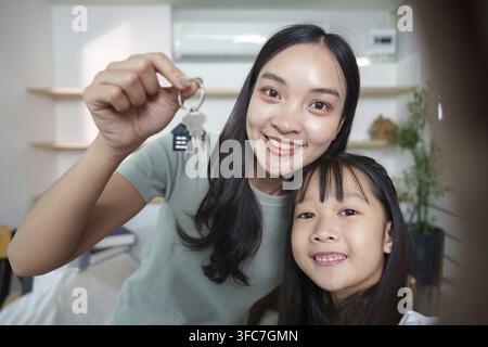Una madre allegra e sua figlia condividono un momento di eccitazione mentre tengono le chiavi della loro nuova casa, che rappresenta nuovi inizi Foto Stock