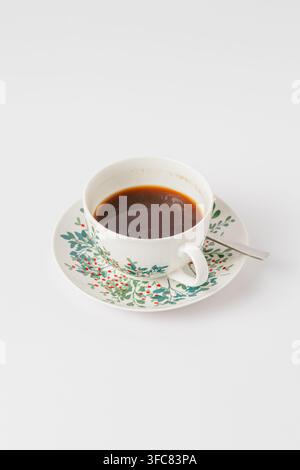 Caffè nero in una tazza di porcellana bianca con sottocoppa a motivi floreali su sfondo bianco Foto Stock