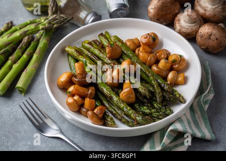 Asparagi arrostiti e funghi interi saltati serviti su un piatto bianco Foto Stock