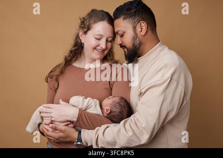 Genitori multirazziali amorevoli che tengono insieme un neonato in un ritratto familiare caldo in studio Foto Stock