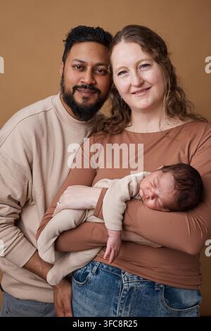 Genitori multirazziali che tengono un neonato in un ritratto familiare caldo e amorevole con toni di pelle diversi Foto Stock