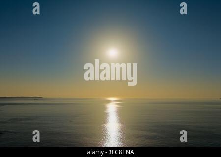Sole luminoso che splende sulle acque calme del Mare d'Irlanda lungo la costa del Pembrokeshire nel Galles, cielo sereno e riflesso di un raggio dorato del sole sulla superficie dell'acqua al tramonto Foto Stock