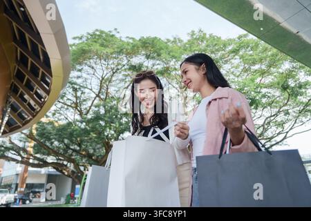 Due donne asiatiche che sorridono mentre guardano nelle borse della spesa all'aperto in un centro commerciale Foto Stock