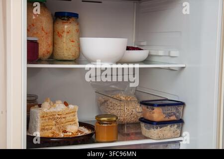 Una varietà di alimenti tra cui barattoli di verdure fermentate, una fetta di torta e contenitori di avanzi sono ordinatamente disposti sugli scaffali di un Foto Stock