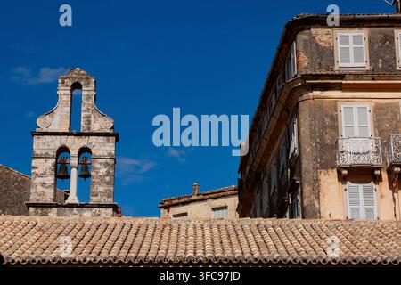 Torre campanaria storica in pietra con due campane in bronzo contro un cielo blu terso, edificio antico della città erosione con finestre dai vetri verdi. Foto Stock